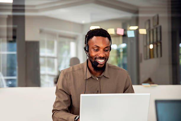 Un conseiller client LokaCI souriant avec un casque audio et micro, travaillant sur un ordinateur portable dans un bureau moderne, pour l'assistance location de véhicules à Abidjan.